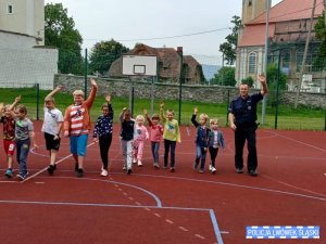 Grupa dzieci wraz z policjantem mają podniesioną rękę i przechodzą po boisku