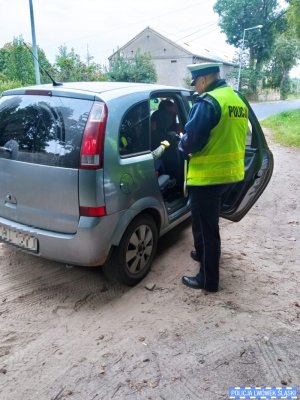 Policjant rozdaje odblaski pasażerom pojazdu, które zatrzymał do kontroli