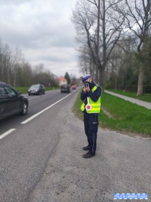 Policjant stojący przy drodze dokonuje pomiaru prędkości