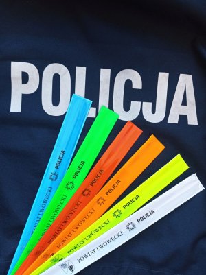 Zdjęcie przedstawia 5 kolorowych opasek odblaskowych na napisie policja