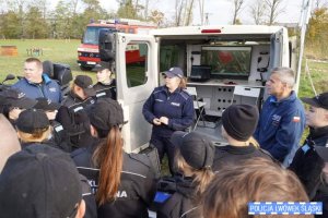 Zdjęcie przedstawia trzech funkcjonariuszy przy busie oraz grupę uczniów