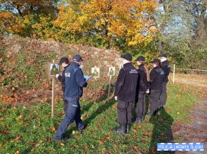 Policjant sprawdza tarcze strzelnicze. Przed tarczami stoi grupa uczniów