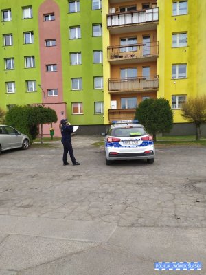 Policjantka stoi pod blokiem z telefonem i sprawdza kwarantanny