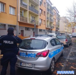 Policjant stoi pod blokiem z telefonem i sprawdza kwarantanny