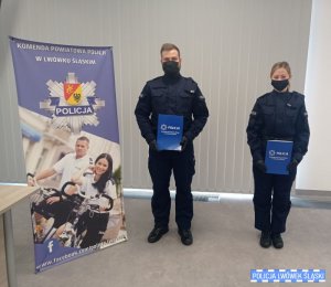 Policjant i policjantka z aktami ślubowania stoją w sali konferencyjnej