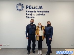 Zdjęcie przedstawia komendanta, policjantkę i dziewczynkę w sali konferencyjnej