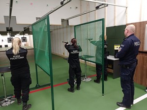 Zdjęcie przedstawia trzy uczennice które strzelają i nadzorującego policjanta