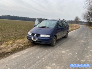 Zdjęcie przedstawia granatowy samochód osobowy na drodze wśród pól