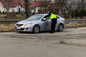 Zdjęcie przedstawia policjanta przy srebrnym aucie podczas badania alkomatem