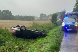 Pojazd osobowy na dachu. Na drodze stoi radiowóz