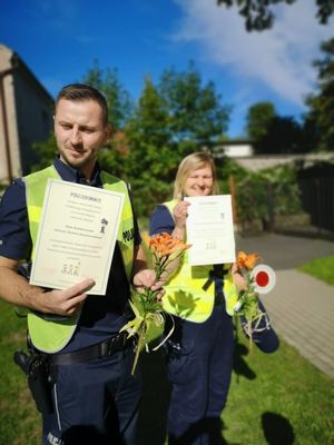 Policjanci stoją z otrzymanymi podziękowaniami i kwiatkami