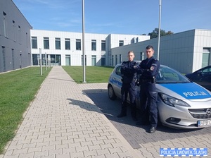 Dwóch policjantów na tle radiowozu i komendy