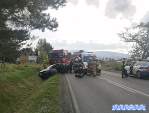 Zdjęcie z miejsca wypadku. Dwa rozbite pojazdy, strażacy i policjanci