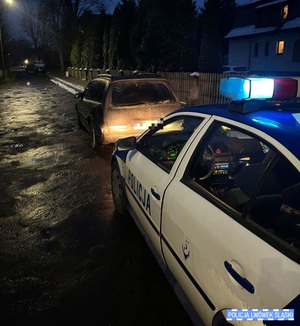 Ciemny pojazd osobowy zatrzymany przez policjantów. Radiowóz stoi za zatrzymanym pojazdem