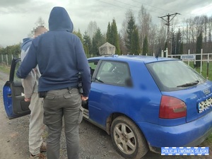 Policjant bez munduru stoi z zatrzymanym przy niebieskim samochodzie