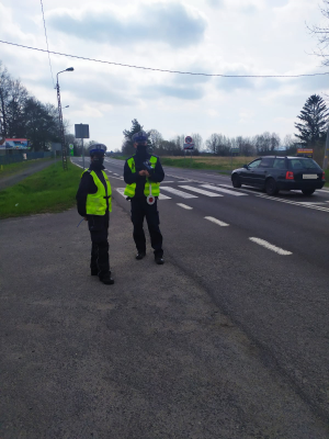 Zdjęcie przedstawia dwoje policjantów ruchu drogowego w odblaskowej kamizelce, którzy stoją przy drodze i obserwują ruch kołowy