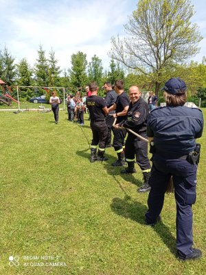 Zdjęcie przedstawia strażaków i policjantkę po jednej stronie liny oraz na przeciwko grupę dzieci podczas zabawy w przeciąganiu liny