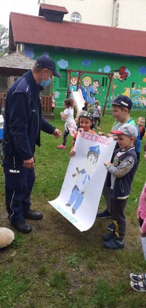 Zdjęcie przedstawia moment gdy trzej chłopcy przekazują policjantowi narysowany plakat