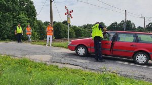 Zdjęcie przedstawia policjanta przy czerwonym pojeździe oraz trzech funkcjonariuszy sok